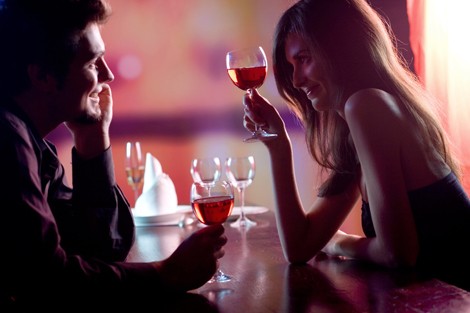 Young couple sharing a glass of red wine in restaurant, celebrating or on romantic date. Focus on woman with glass.