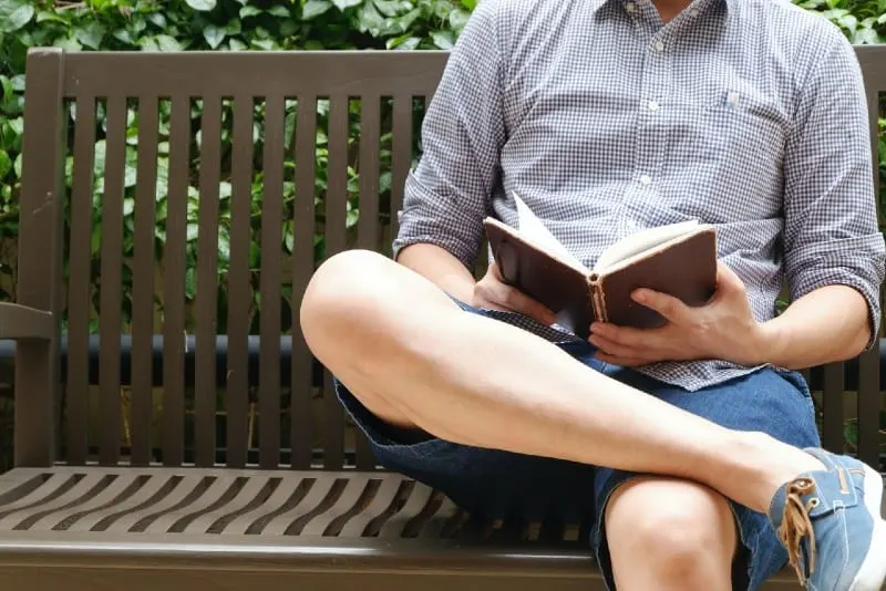 man reading book while sitting on bench