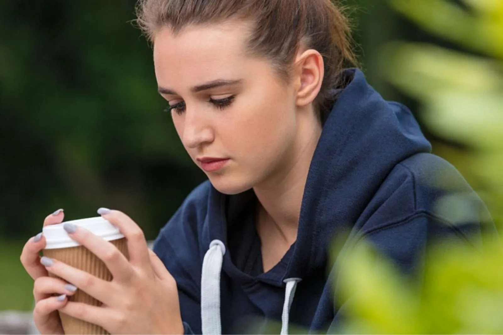 sad pensive woman wearing a blue hoodie sitting and holding a cup of coffee