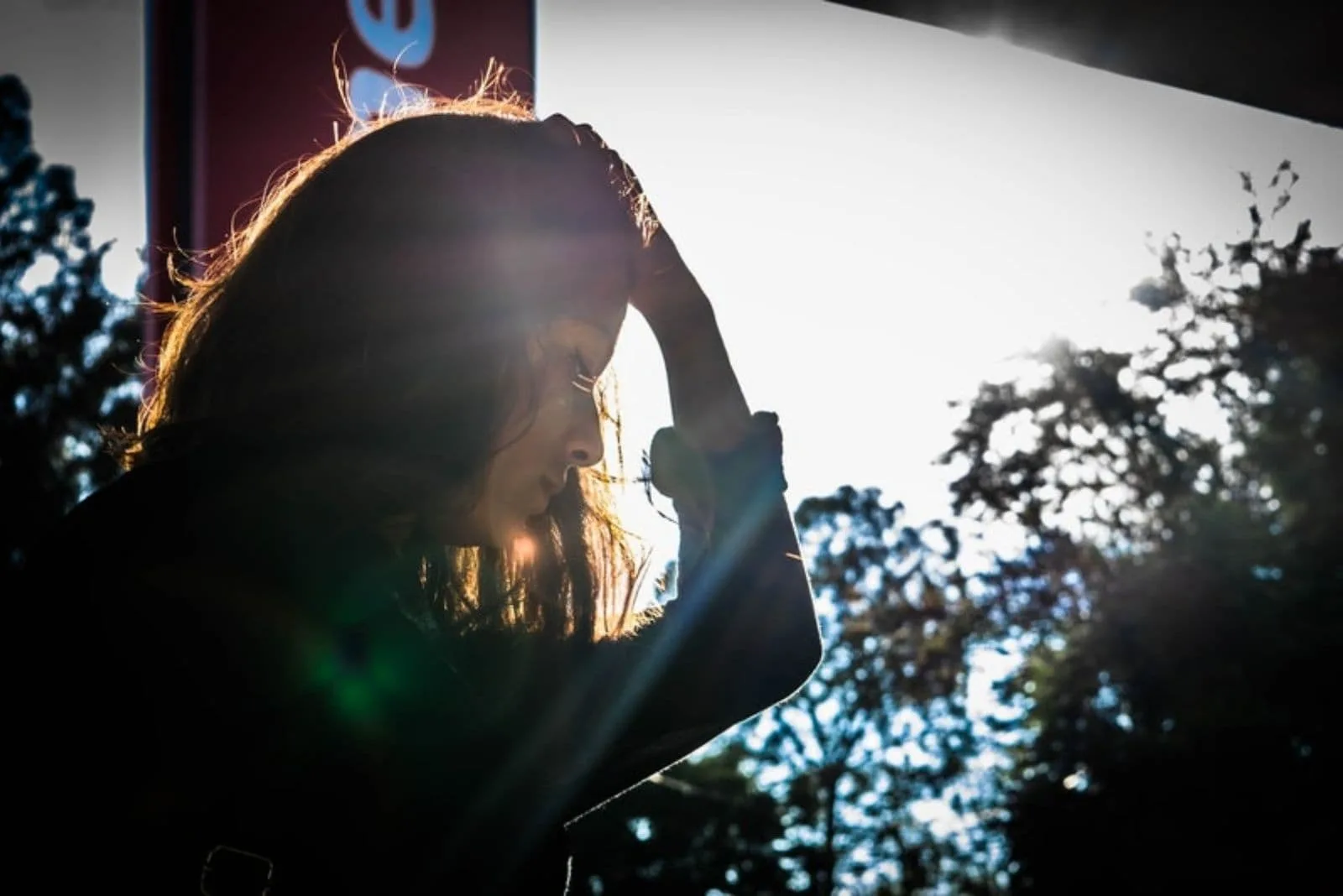 sad pensive young woman holding her head standing near the glass windows with a the ray of the sun coming in