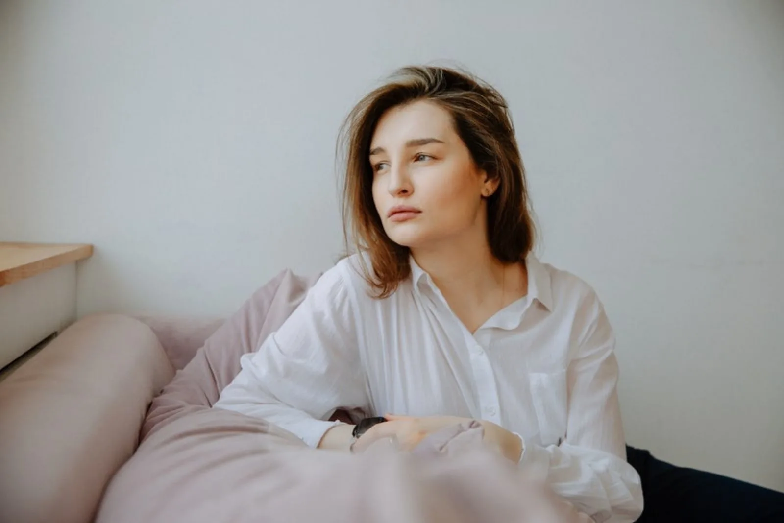 young woman wearing white polo leaning on the couch thinking and looking away