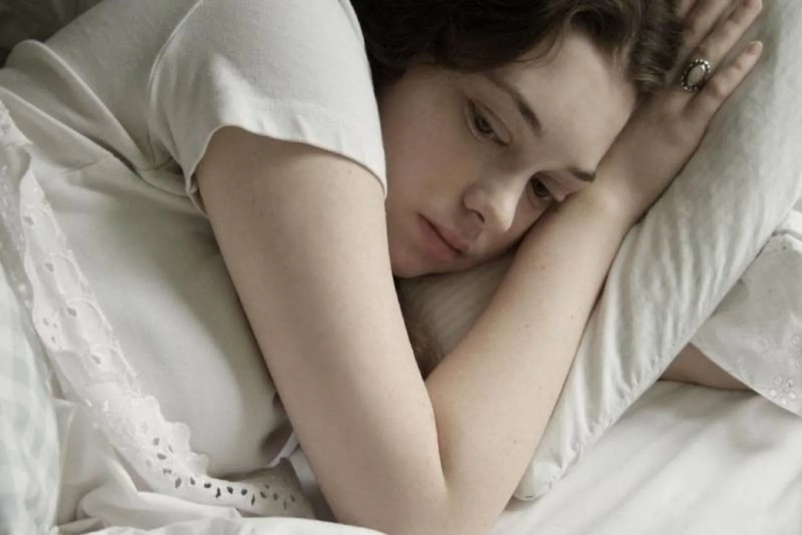 tired pensive woman lying down in bed facing her left side of the bed