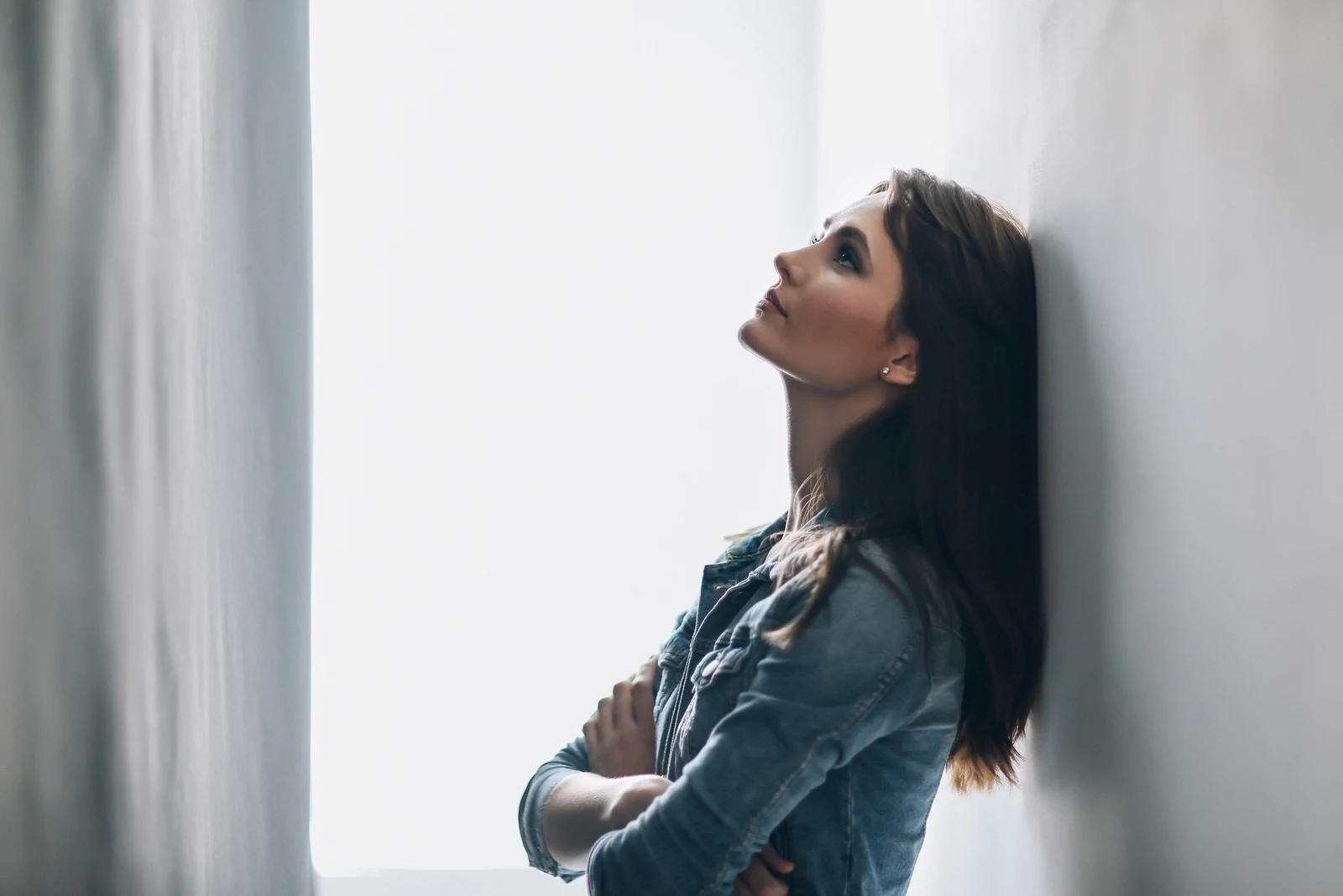the woman stands pensively leaning against the wall