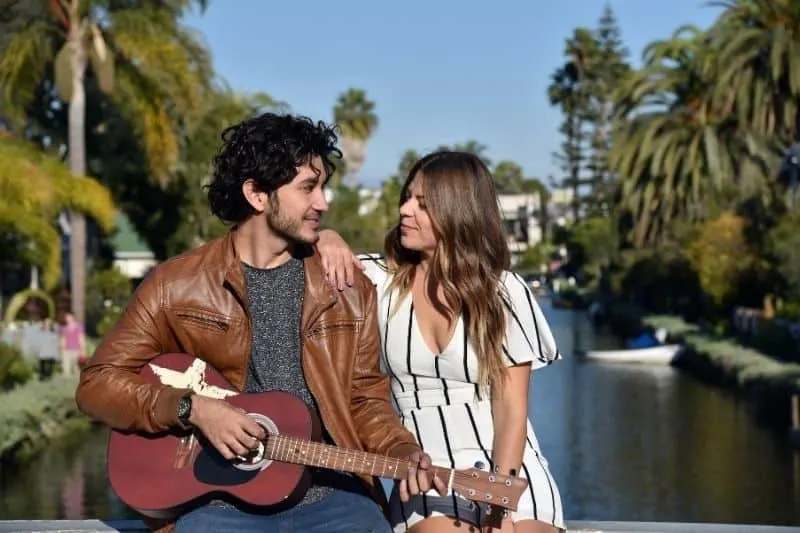 60 des meilleures idées pour complimenter un homme sur sa personnalité 11 handsome man playing guitar with a woman smiling and sitting near the river bank