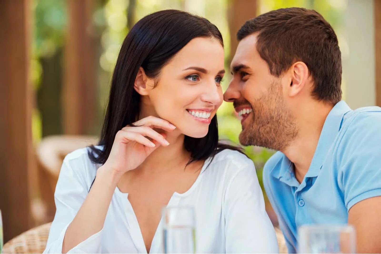the man whispers in the ear of a smiling woman